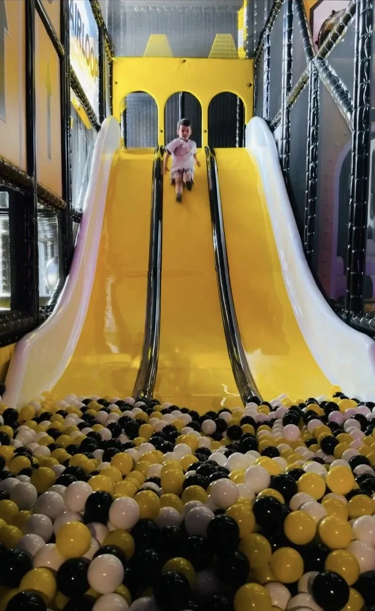 Enfant descendant un grand toboggan jaune dans la piscine à balles d'AIRKIDS chez Airloop, Grand-Lancy