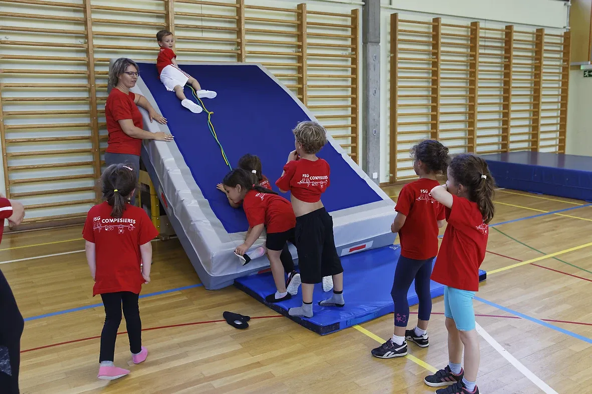 Enfants en t-shirt rouge grimpant sur un module de gym encadrés par une monitrice dans une salle de sport genevoise