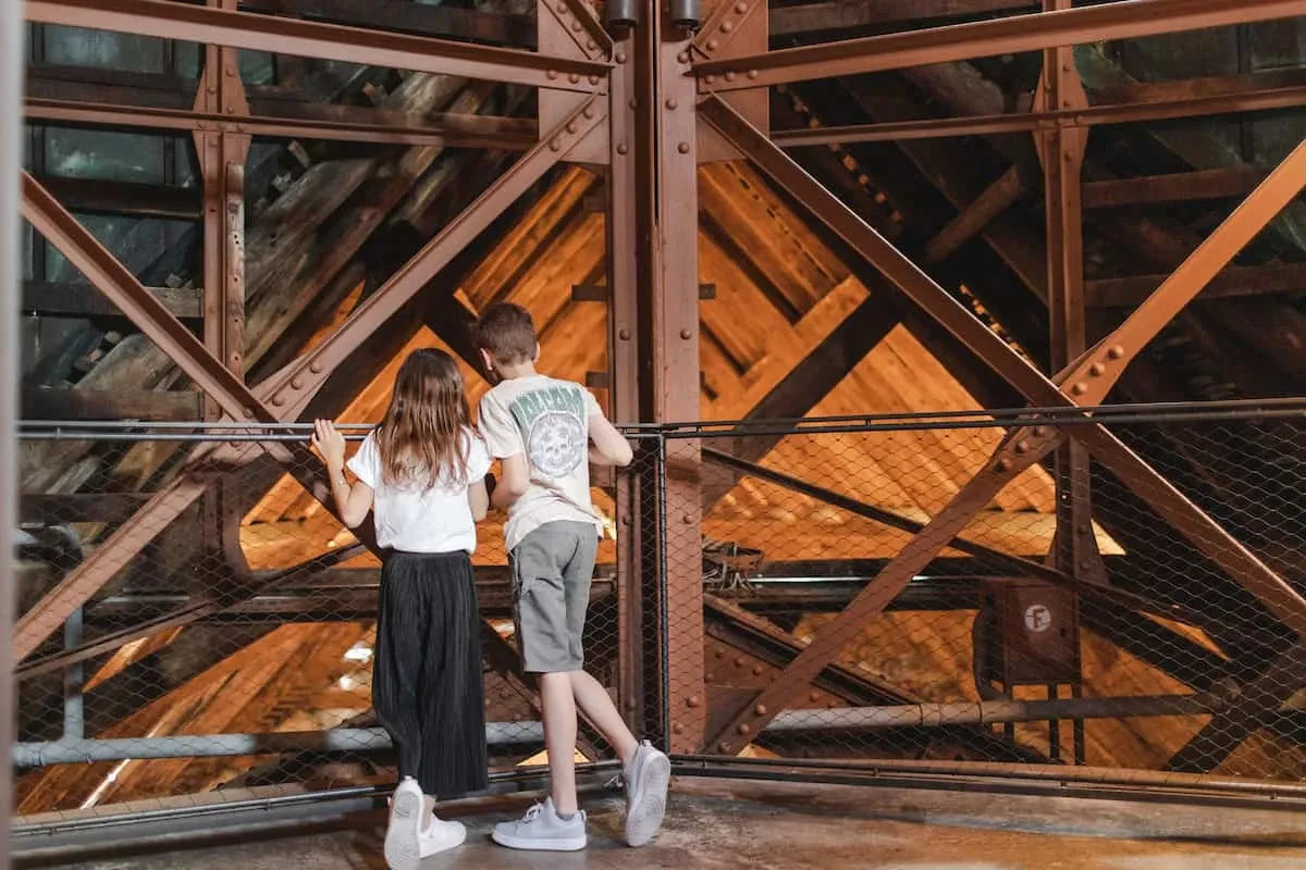 Deux enfants observent la charpente et les cloches depuis l'intérieur des tours de la Cathédrale Saint-Pierre à Genève.