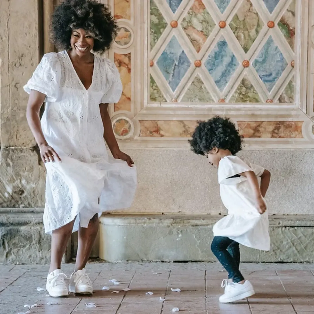 Mère et jeune enfant qui dansent ensemble en tenue blanche, sourires complices.