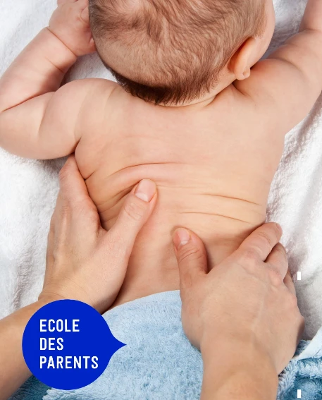 Mains d'un parent massant doucement le dos d'un nourrisson allongé sur une serviette blanche.
