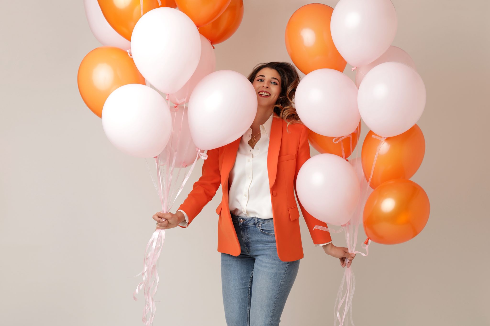 Femme souriante tenant de grands bouquets de ballons orange et rose pâle à l'hélium