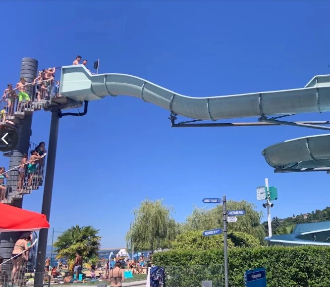 Toboggan aquatique de Genève-Plage avec baigneurs et lac Léman en arrière-plan, par beau temps