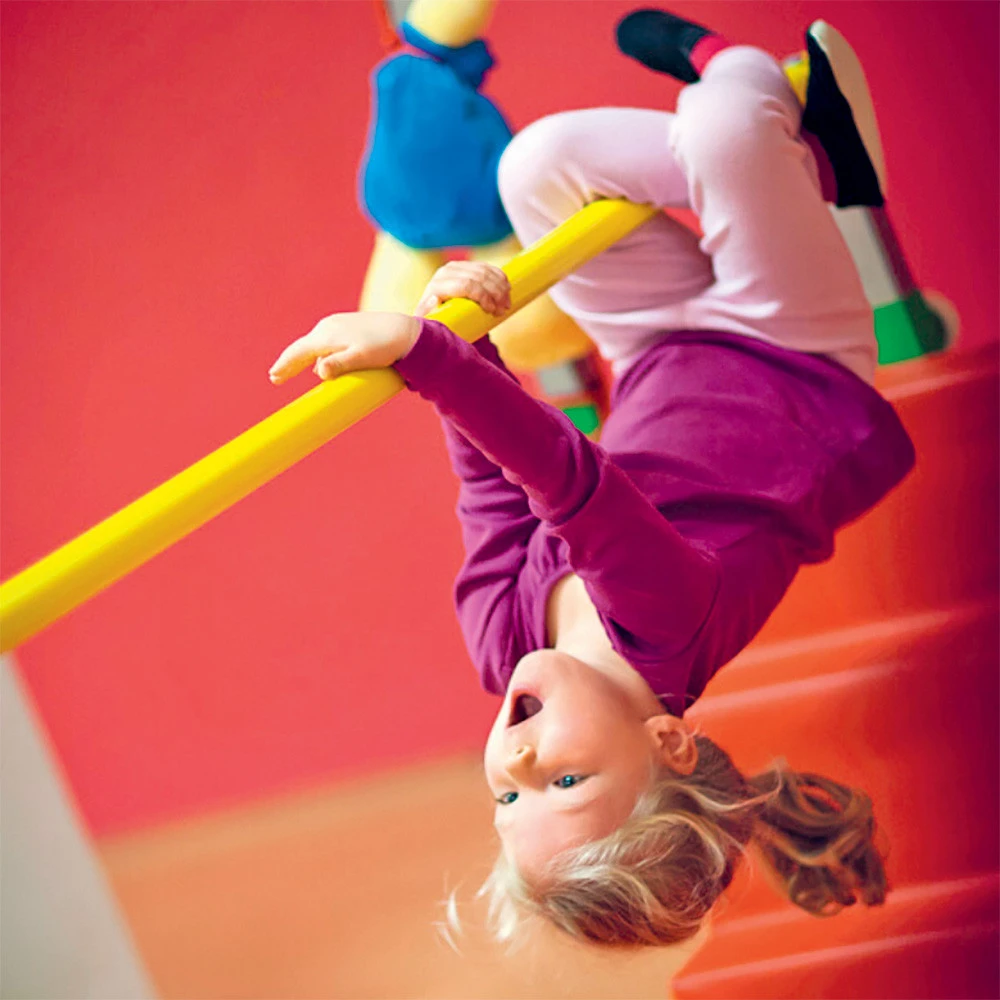 Petite fille suspendue tête en bas à une barre jaune lors d'un cours de baby gym