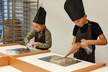 Deux enfants en toque et tablier réalisent une tablette de chocolat lors d'un atelier à Genève