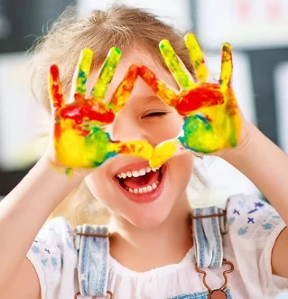 Petite fille souriante les mains couvertes de peinture colorée lors d'un atelier créatif