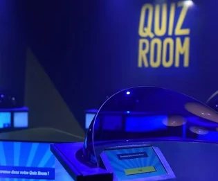 Plateau de jeu de la Quiz Room à Genève, avec buzzers éclairés en bleu et enseigne lumineuse Quiz Room