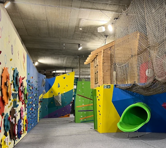 Zone kids de TOTEM Meyrin avec murs d'escalade colorés, cabane en bois, filet en hauteur et toboggan vert.