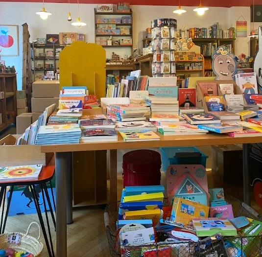 Intérieur de la librairie Au Chien Bleu à Genève, table couverte d'albums jeunesse colorés et jeux en arrière-plan.