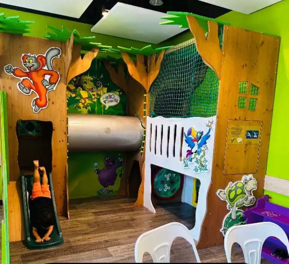 Espace de jeux intérieur du Coop Bistro Onex avec toboggan et structure en bois sur le thème de la jungle