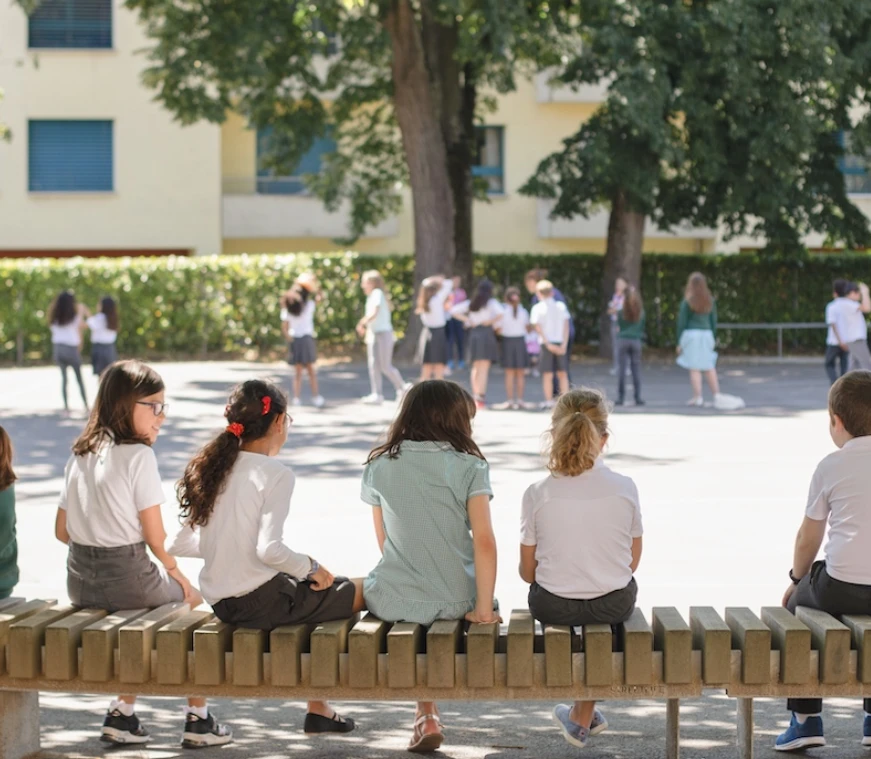 Élèves de l'Institut International de Lancy assis dans la cour de récréation ensoleillée du campus