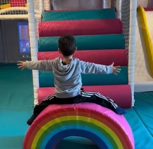 Enfant assis sur un arc-en-ciel coloré dans le playground intérieur de Just Bloom à Genève