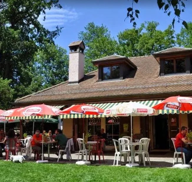 Terrasse ensoleillée du Restaurant du Tennis Club d'Onex avec parasols colorés et jardin verdoyant
