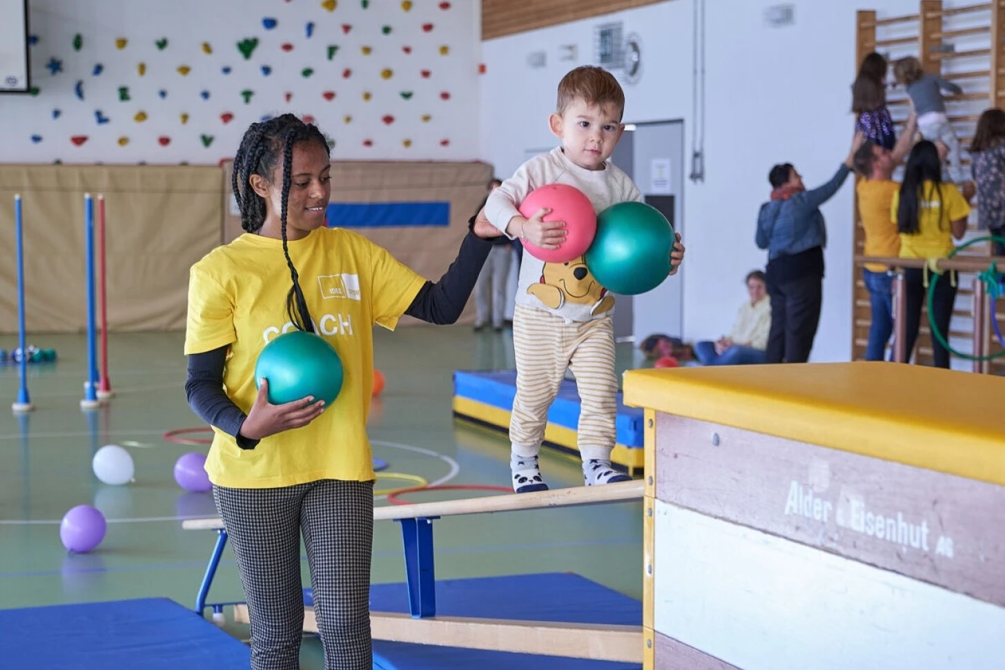 Coach idée Sport guidant un jeune enfant sur un banc de gym lors d'une séance MiniMove